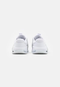 Witte sportieve schoenen met een gladde, textuur bovenkant, een trekhaak aan de hiel en grijze accenten op de zool voor grip en ondersteuning.