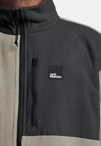 Fleece-Zipjacke in Schwarz und Hellgrau. Mit hohem Kragen, taschiertem Reißverschluss und einem Logo-Patch auf der Vorderseite. Weiche Textur.