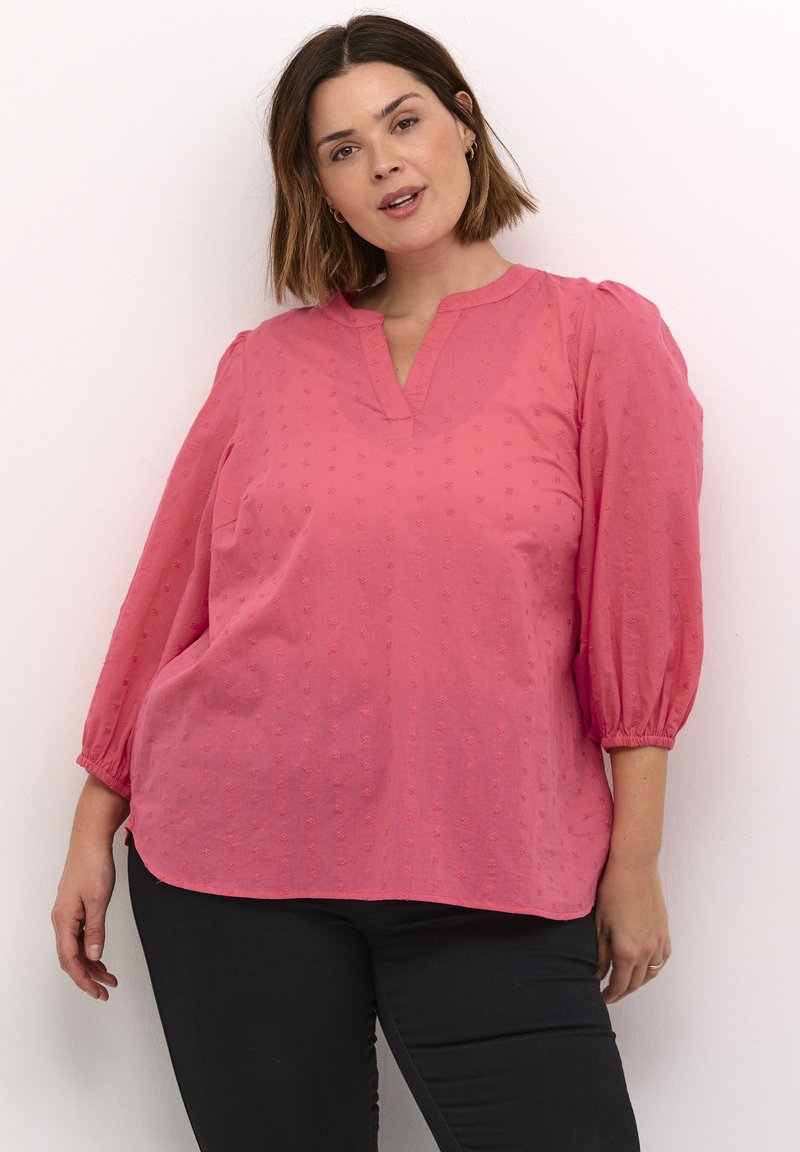 Blouse rosa realizzata in tessuto leggero con pois testurizzati, maniche a sbuffo 3/4 e scollatura a V. Presenta una vestibilità rilassata e spacchi sui lati.