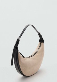 Sac hobo en tissu beige avec une base et une bandoulière en cuir noir, présentant une forme incurvée et une fermeture éclair sur le dessus.