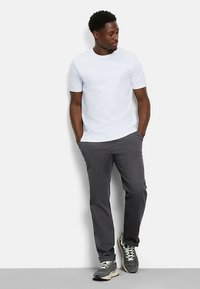 Weißes T-Shirt mit kurzen Ärmeln, kombiniert mit grauen Slim-Fit-Hosen und schwarzen Sportschuhen. Der Stoff wirkt glatt, mit einer lässigen Passform und sauberem Design.