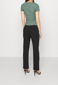 Grön ribbad topp med kort ärm som matchas med svarta byxor. Byxorna har en rak bendesign och bakfickor. Svarta högklackade sandaler.