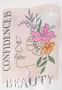Graphic T-shirt featuring a line drawing of a face with floral accents in pink, orange, and green. Text reads "Confidence is Beauty" in silver.