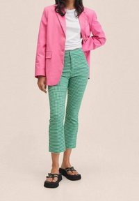 Roze blazer over een witte t-shirt, gecombineerd met groene geruite broeken en zwarte platform sandalen. De outfit heeft verschillende patronen en texturen.
