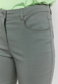 Grijze denim jeans met een getailleerd ontwerp, voorzien van een voorknoopzak en een gladde textuur. De tailleband heeft een knoopsluiting en riemlussen.