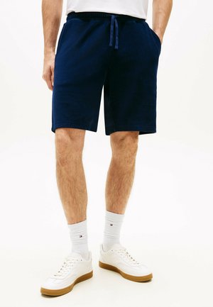 Mand iført marineblå shorts med snøre, hvide sneakers med gummisåler og hvide mellemlange sokker med et lille logo.