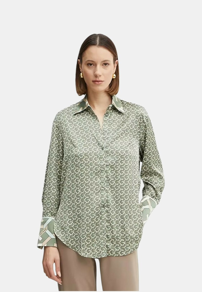 Camisa verde con estampado, con cuello clásico, mangas largas y puños contrastantes que presentan un diseño geométrico. Textura de tela suave.