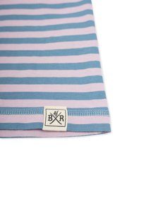 Raidallinen kangas, jossa vuorottelevat vaaleansiniset ja vaaleanpunaiset värit, ommeltu helma ja suorakulmainen tagi, jossa on alustavan "B/R".