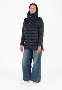 Marineblauwe pufferjack met hoge kraag en gouden rits, heeft een gestikte ontwerp, lange mouwen en een slim fit. G.combineerd met wijde jeans en witte sneakers.