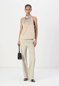 Top halter beige con dettagli plissettati, abbinato a pantaloni a gamba larga beige chiaro. Gli accessori includono una piccola borsa nera e tacchi aperti.
