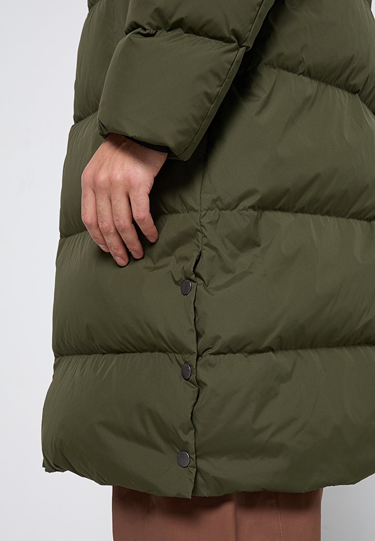 Olivgrüne Puffjacke mit gestepptem Muster, ausgestattet mit einer einzelnen Reihe schwarzer Druckknöpfe an der Seite und einem designed Bündchenärmel.
