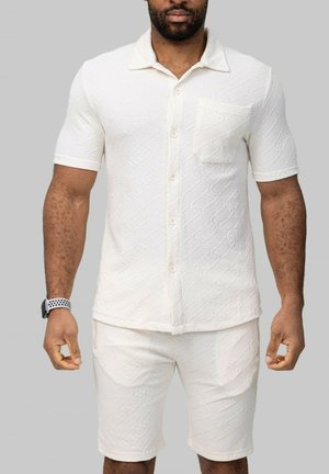 Chemise blanche à motifs avec des manches courtes et une poche, assortie à un short ; tissu texturé avec un design géométrique.