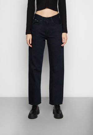 Tummansiniset leveät farkut, joissa on korkea vyötärö, viisi taskua ja ommeltua yksityiskohtaa. Yhdistettynä lyhytmustan topin ja mustien kenkien kanssa.