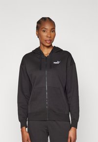 Felpa nera con zip realizzata in tessuto morbido, con tasca a marsupio, coulisse regolabile e un piccolo logo Puma bianco sul petto.