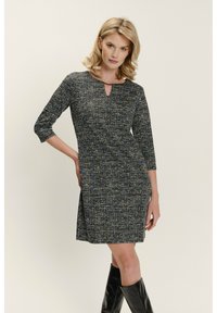 Knee-length šaty s texturovanou tkaninou, která má tmavě modrý a bílý vzor, 3/4 rukávy a detail výstřihu ve tvaru klíčové dírky.