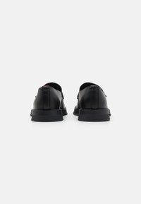 Chaussures noires en cuir à lacets avec une finition lisse, bout rond et semelle en caoutchouc basse. Présentent des détails cousus et un accent subtil à l'arrière.