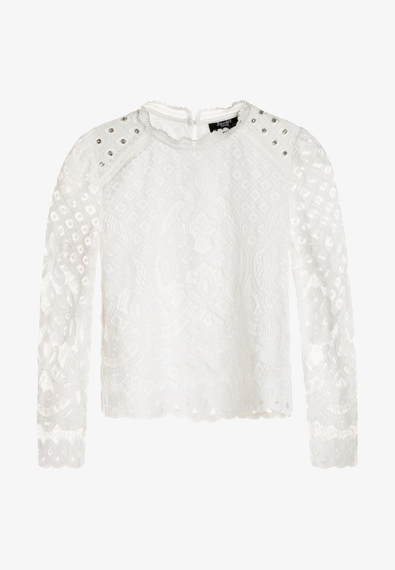 Blouse en dentelle blanche à manches longues, motifs floraux complexes, ourlet festonné et clous argentés sur les épaules. Dos ouvert avec fermeture à trou de serrure.