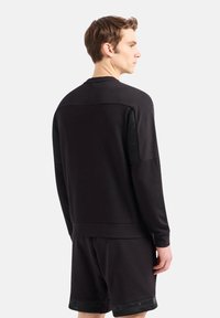 Felpa sportiva nera con colletto a girocollo, caratterizzata da inserti in rete sulle spalle. Abbinata a pantaloni corti neri coordinati.