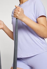 Světlofialové sportovní tričko s krátkým rukávem, doplněné o odpovídající šortky. Držení šedé odporové gumy, která ukazuje hladkou strukturu látky.