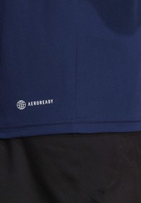 Mörkblå sporttröja med mesh-textur, med "AEROREADY"-logotyp i vitt, kombinerad med svart tyg under, visar en sömlös design.