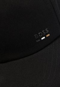 Fekete szövet baseballsapka, az elülső panelen kiemelkedő "BOSS" logóval fekete, fehér és barna színekben.