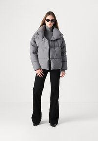 Grå pufferjakke med en bred krave, oversized form og frontlommer. Båret over en grå turtleneck og kombineret med sorte flared bukser.