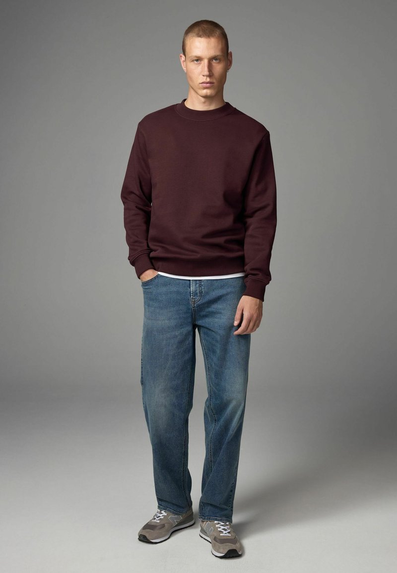 Sudadera burdeos con cuello redondo, corte relajado. Jeans de pierna recta azules claros. Zapatillas deportivas beige con detalles grises. Texturas suaves.