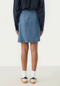 Jupe en denim, lavage moyen, longueur genou, forme évasée, ourlet brut, associée à des chaussettes blanches et des baskets décontractées pour un look détendu.