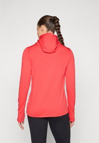 Czerwony, teksturowany sweatshirt z kapturem, długimi rękawami i otworami na kciuki, o dopasowanym fasonie i lekko zaokrąglonym zakończeniu.