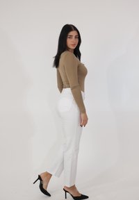 Beżowy, dopasowany top z długim rękawem w połączeniu z białymi, wysokim stanem jeansami. Czarne buty na obcasie. Gładka faktura bez widocznych wzorów. Prosty design.