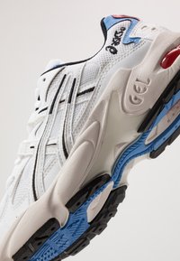 Vit sport sneaker med mesh- och syntetmaterial, svarta och blå accenter, synlig dämpning och texturerad gummiyttersula.