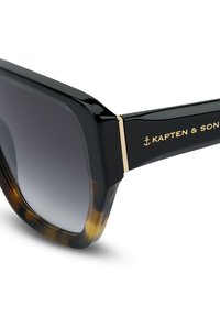 Neliön muotoiset aurinkolasit, joissa on kiiltävä musta sääntö ja kilpikonnakuvioiset yksityiskohdat. Tummat gradienttimuotoiset linssit ja kultaiset yksityiskohdat.