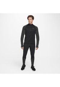 Schwarzes Sportset mit einem langärmligen Zip-Up-Oberteil mit strukturierten grauen Akzenten und einer enger geschnittenen Hose mit gemusterten Bündchen.