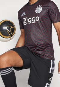 Červeno-černý fotbalový dres se vzorem a logem "Ziggo", černé šortky s bílými pruhy a černý a zlatý fotbal.
