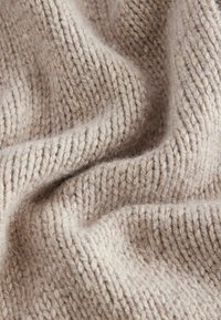 Tissu beige doux en tricot avec des coutures côtelées visibles et des plis doux créant texture et profondeur.