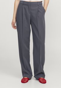 Šedé široké kalhoty se skládanými nohavicemi a bočními kapsami, spárované s jasně červenými síťovými slip-on botami. Hladká látka, módní střih.