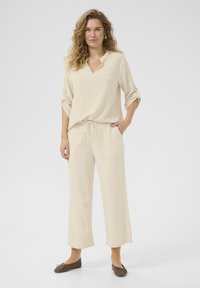 Beige Leinenmischung Oberteil mit V-Ausschnitt und dreiviertel Ärmeln, kombiniert mit passenden Jogginghosen mit Kordelzug. Enthält flache braune Schuhe.