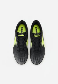 Zapatillas deportivas negras con un upper texturizado, acentos en verde lima, patrón de puntos y cordones negros. Logo de Diadora visible en la plantilla.