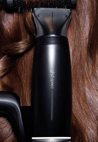 Sèche-cheveux noir ghd Speed coiffant de longs cheveux bruns brillants avec une brosse ronde enroulant une mèche.