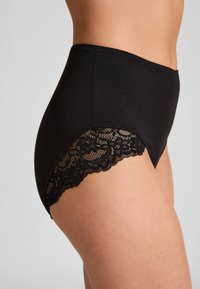 Zwarte, hoog uitgesneden ondergoed met een elastische tailleband en bloemenkant langs de beenopeningen. Glad materiaal met een ademende textuur.