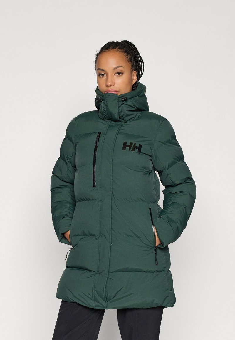 Cămașă puffer de culoare verde închis, cu guler înalt, închidere cu fermoar, două buzunare laterale și detaliu cu logo pe piept. Oferă un design matlasat și o textură netedă.