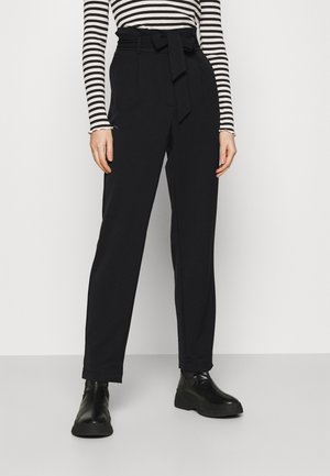 Persoon met een zwarte broek met hoge taille en een strikceintuur, gecombineerd met een zwart-wit gestreept langarmshirt en zwarte enkellaarzen.