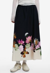 Zwarte bloemenrok met een levendige bloemenprint aan de zoom, een gerimpelde elastische tailleband en een zachte stofstructuur. Gecombineerd met beige schoenen.