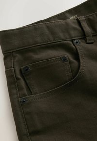 Pantalon en denim vert foncé avec une poche avant présentant des rivets noirs visibles et un passant de ceinture au-dessus de la ceinture.