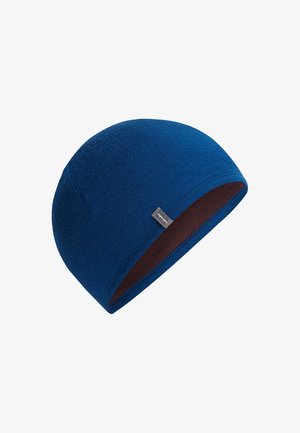 Gorra de punto azul con una pequeña etiqueta negra, mostrando una forma ligeramente curvada y un forro interior marrón.