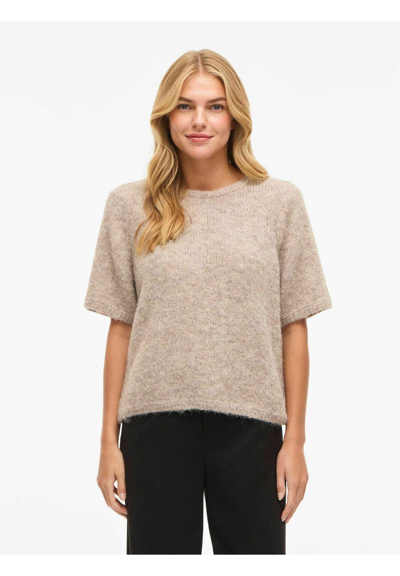 Beež lühikeste varrukatega kampsun, pehme ja tekstuurse kudumiga, ümar kaelusega ning veidi lühem lõige. Sobitatud tumedate pükstega.