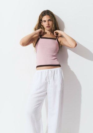 Light pink tank top with thin straps and dark brown trim, paired with loose white linen pants, showcasing a relaxed fit.