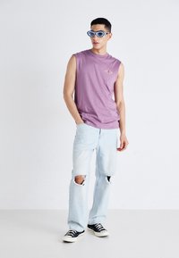 Purple sleeveless t-shirt with a small graphic, light blue ripped jeans, and black sneakers, complemented by blue sunglasses.