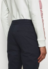 Navy jogger pants with elastic waistband, side pockets, and a subtle texture. Paired with a light-colored long-sleeve top.