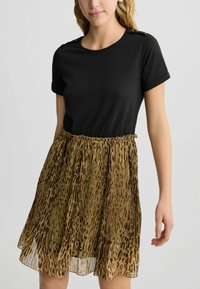 Top nero a maniche corte con dettagli in oro alle spalle, abbinato a una gonna plissettata di lunghezza ginocchio con un motivo nei toni del marrone e beige.